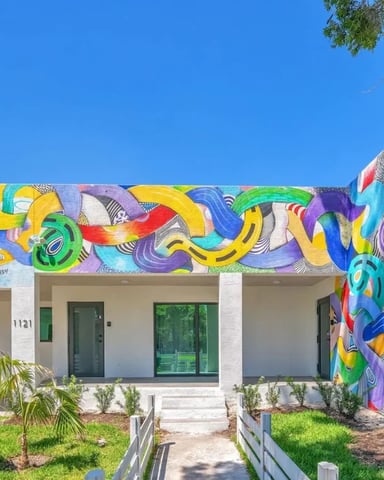 Modern white house with vibrant colorful graffiti mural, green doors, and large tree in front yard
