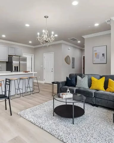 Open-plan living room and kitchen with gray sectional sofa, dining table, white cabinetry, and crystal chandelier
