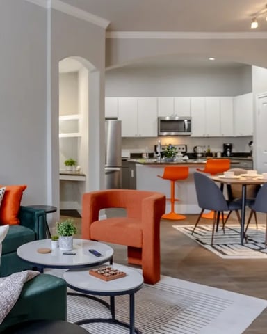 Open-plan living room with teal sofa, orange accent chair, and dining area with kitchen visible beyond