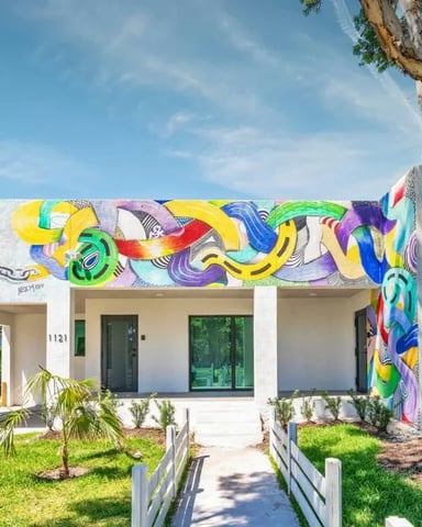 Modern white house with colorful abstract mural, large tree, manicured lawn, and white fence pathway