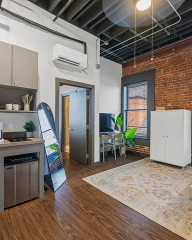 Modern loft studio with exposed brick, open kitchen, hardwood floors, and city views through large windows