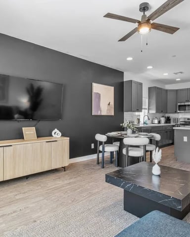 Open-plan living room and kitchen with dark gray walls, wood credenza, marble coffee table, and dining area with bar seating.