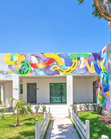 Modern white house with vibrant colorful mural, large tree, and manicured lawn with walkway