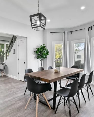 Bright dining room with wood table, black chairs, pendant light, and glass doors opening to deck