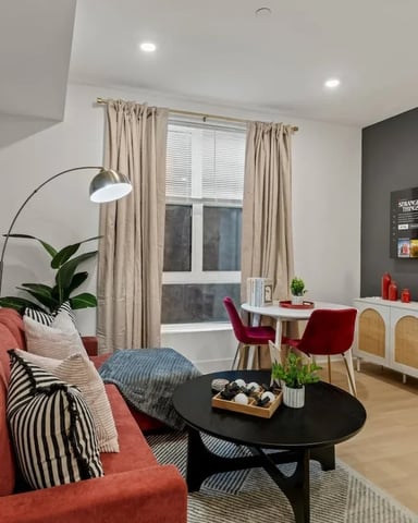 Modern living room with red sofa, black coffee table, wall-mounted TV, white credenza, and large window with beige curtains