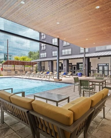 Indoor pool area with yellow seating, dining tables, and wood-ceiling pavilion overlooking urban courtyard.