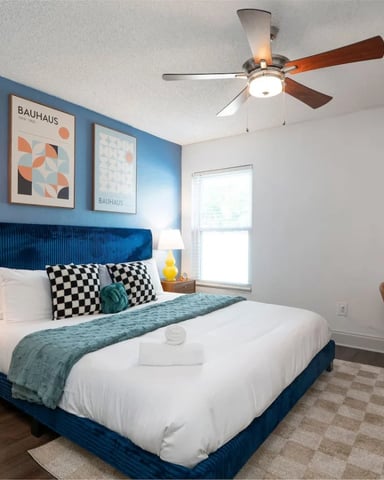 Modern bedroom with blue accent wall, blue upholstered bed, yellow lamps, mid-century wood nightstands, and desk with chair