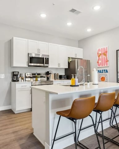 Modern kitchen with white cabinetry, stainless steel appliances, large island with tan leather bar stools, and wood flooring